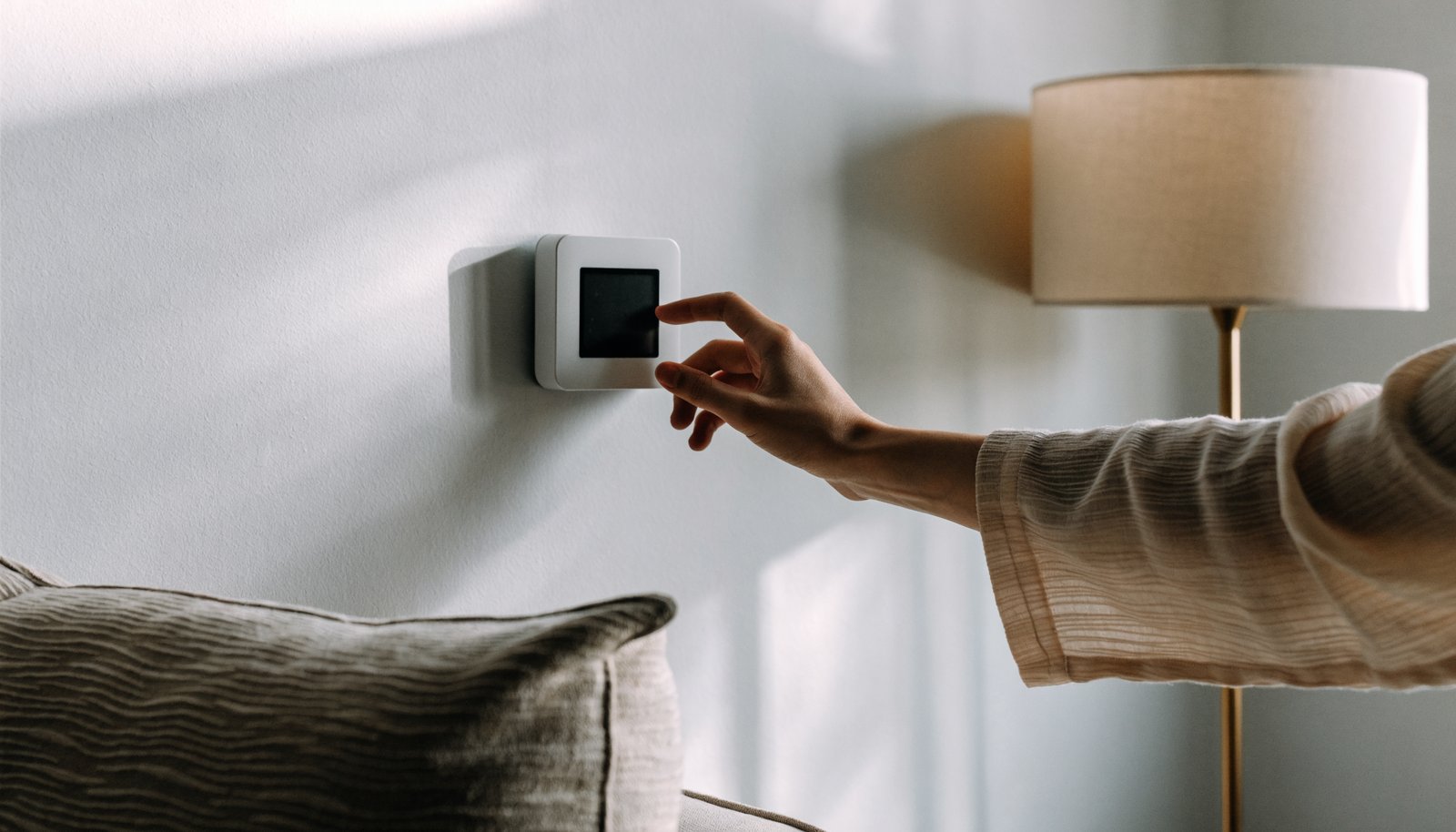 Hand adjusting a small square smart thermostat mounted on a living room wall