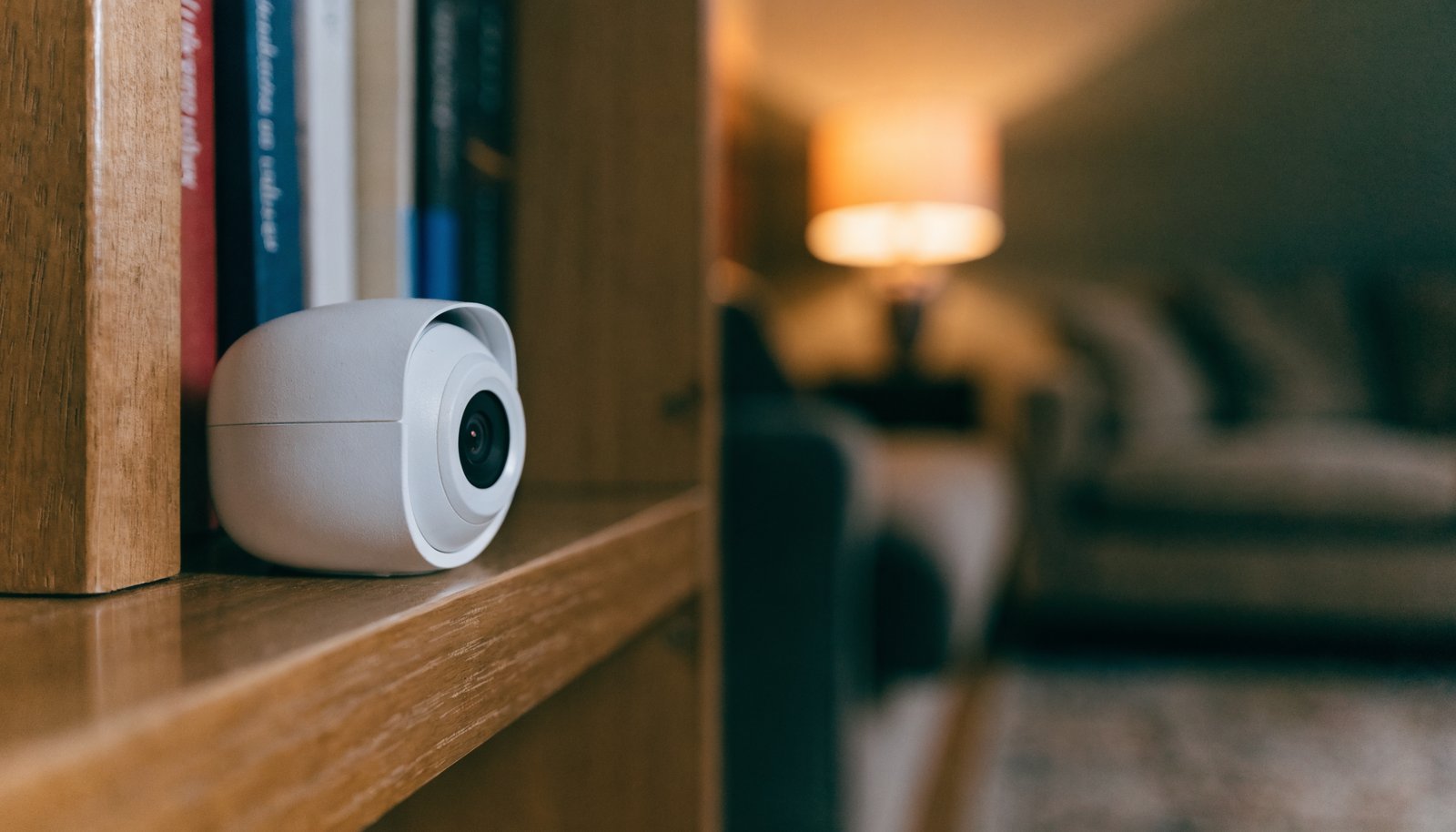 Small white indoor security camera on a bookshelf facing a lamplit living room